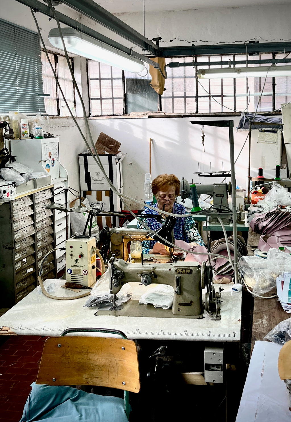 Blick in das lichtdurchflutete Näh-Atelier der Schuh-Manufaktur nahe Civitanova Marche, wo die Schuhe von Stefi Talman hergestellt werden. Das Bild zeigt die Mutter des Unternehmers bei der Arbeit an der Nähmaschine.